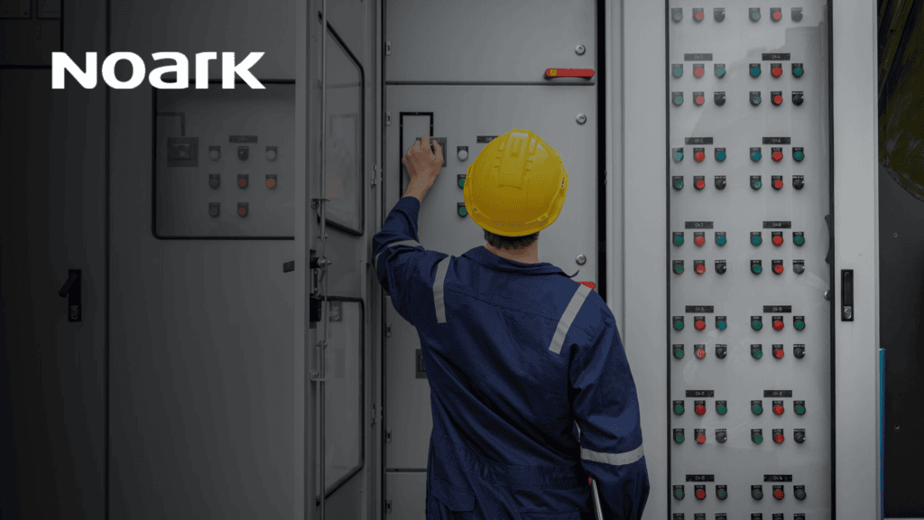 Un trabajador con uniforme azul y casco amarillo maneja con destreza un panel de control, garantizando el perfecto funcionamiento de los sistemas de contacto por relé en una instalación industrial. El logotipo "Noark" ocupa un lugar destacado en la esquina superior izquierda, resaltando la dedicación de la marca a la calidad y la innovación.