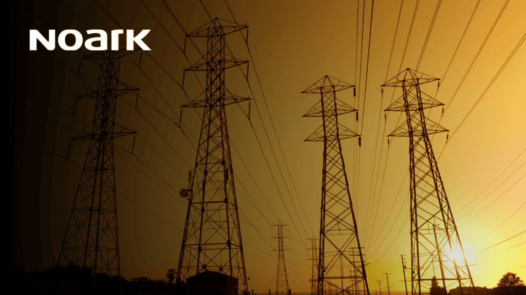 Contra el cielo naranja vibrante del atardecer, las líneas eléctricas y las torres se extienden en el horizonte. La palabra "Noark" adorna la esquina superior izquierda, destacando sutilmente la importancia de los interruptores de desconexión para garantizar el flujo continuo de energía y la seguridad.