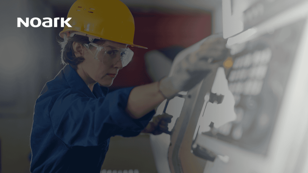 Una persona con casco y gafas de seguridad maneja maquinaria conectada al sistema de control industrial. En la esquina se ve el logotipo de Noark.