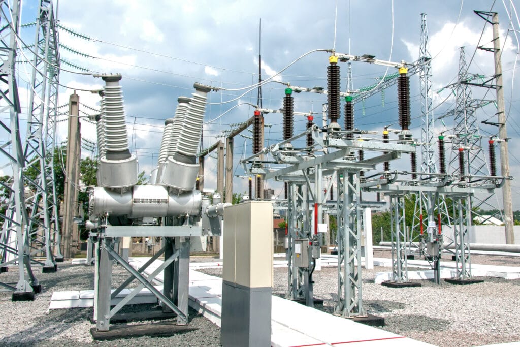 Subestación eléctrica con transformadores, disyuntores y líneas eléctricas bajo un cielo nublado.