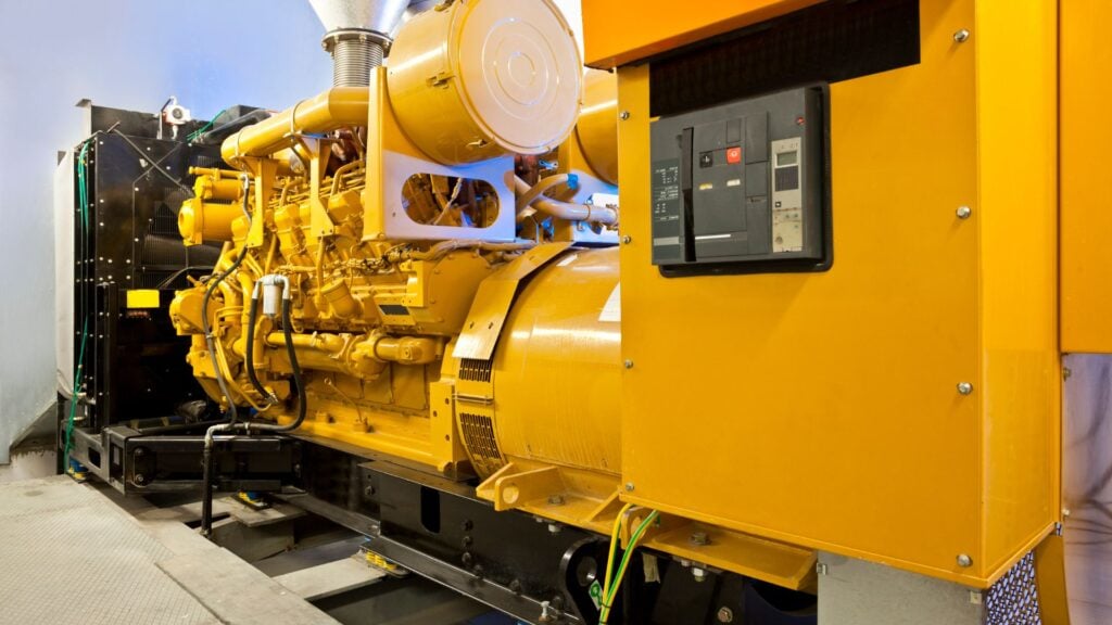 Un gran generador industrial amarillo con un robusto motor se instala en el interior, con un panel de control y varios cables.