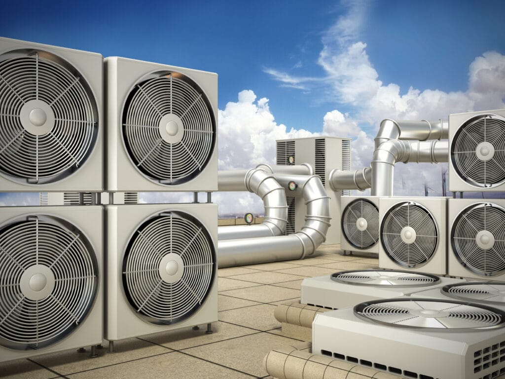 Vista desde el tejado de varias unidades de calefacción, ventilación y aire acondicionado y conductos bajo un cielo azul con nubes, que pone de relieve los entresijos de los sistemas de refrigeración modernos.