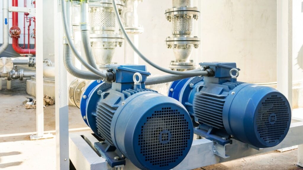 Dos grandes bombas industriales azules con motor están instaladas en una plataforma metálica, perfectamente integradas en el sistema de gestión del agua de la fábrica, conectadas por tuberías y cables.